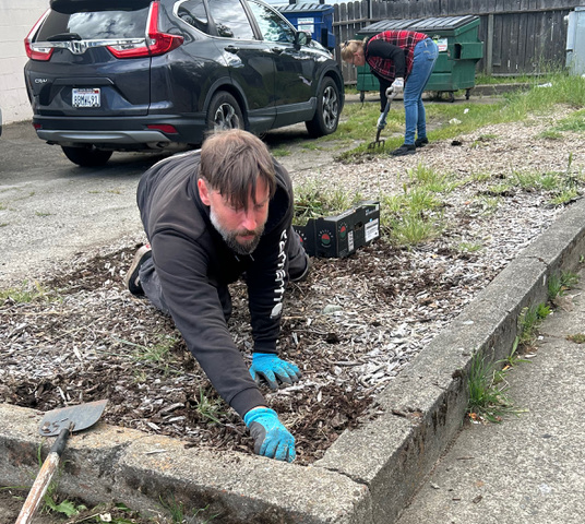 Casey weeding a planter bed at Prime Market alongside a fellow co-op worker